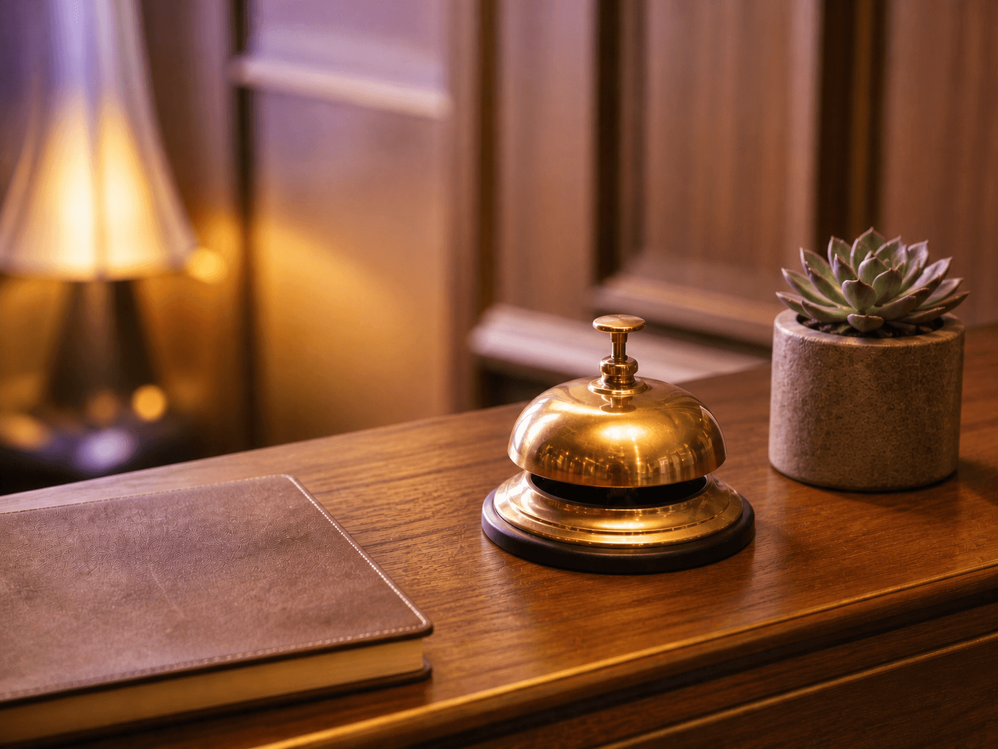 Boutique hotel reception desk with brass bell and succulent under violet ambient light