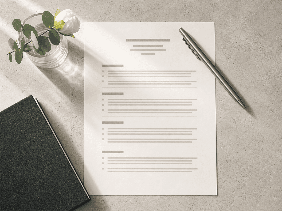 A printed résumé on a warm stone desk with a pen, a notebook and a glass of eucalyptus